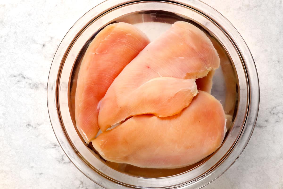process shot showing how to make oven baked chicken breast by brining the chicken in salted warm water in a bowl