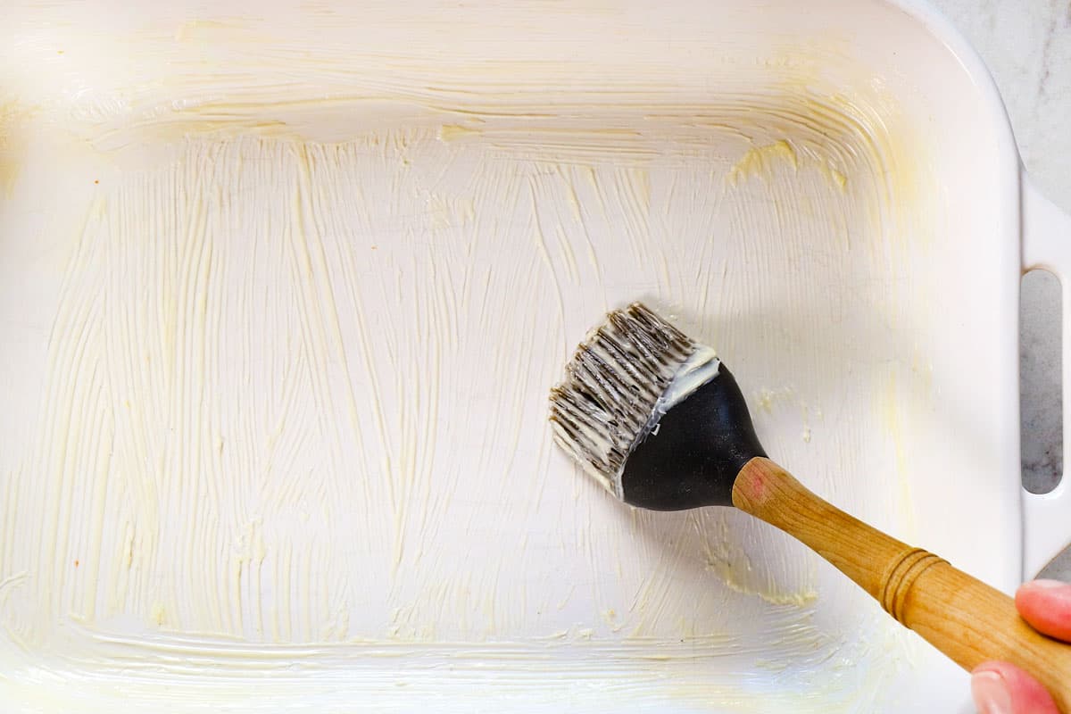 process shot showing how to make oven baked chicken breast by buttering baking dish before adding chicken