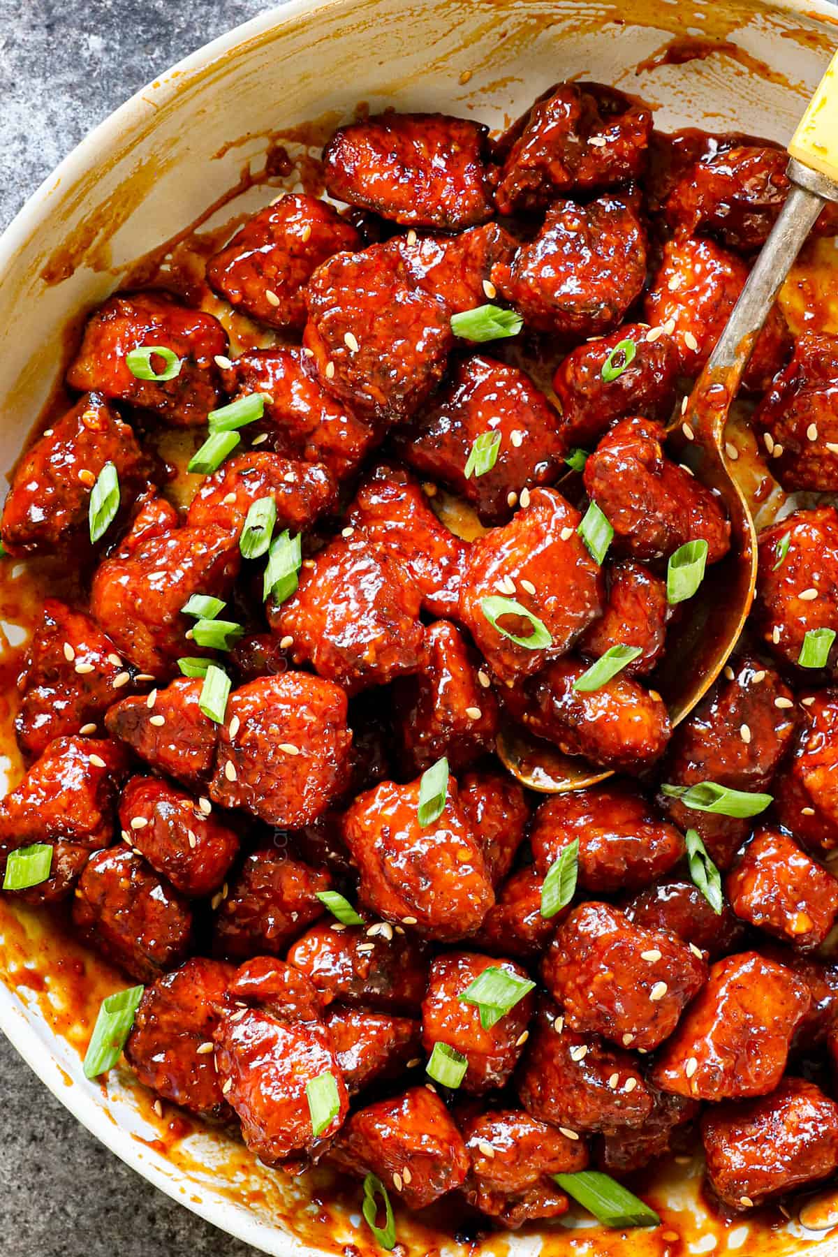 showing how to make Korean fried chicken (yangnyeom) by tossing the chicken with sauce and garnishing with green onions