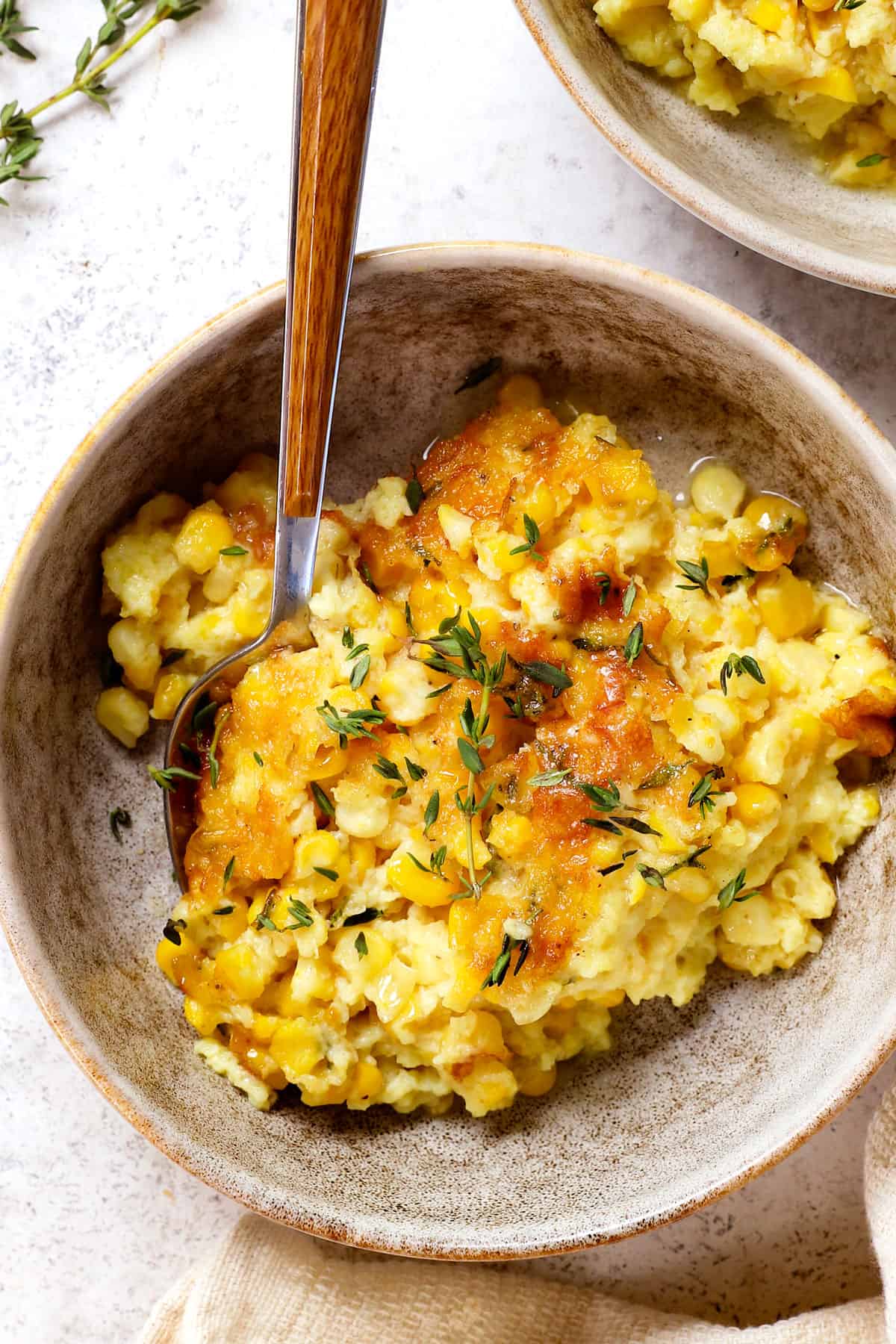 top view showing how to serve corn pudding in a bowl with a spoon garnished with herbs