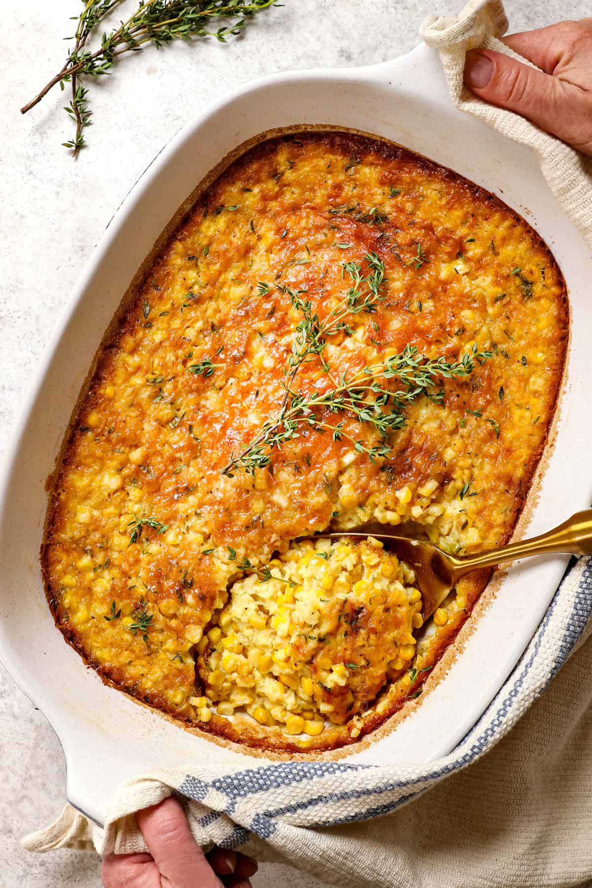 two hands holding corn pudding casserole to serve