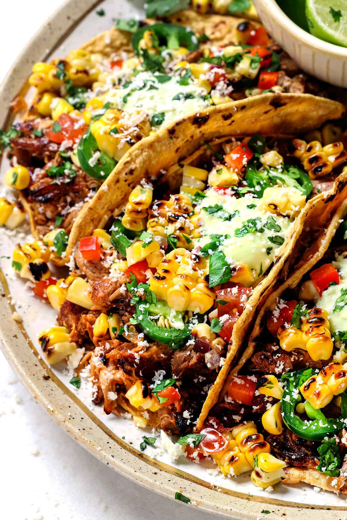 tacos carnitas being served on a plate in corn tortillas with lime wedges