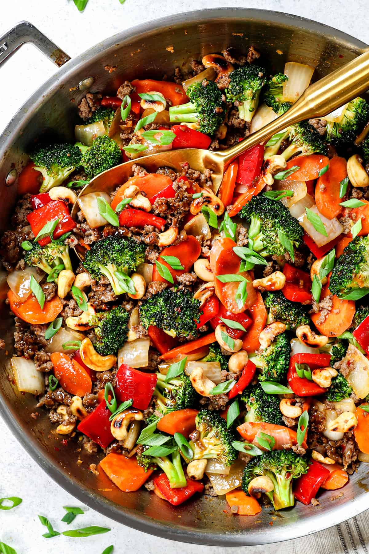 showing how to make stir fry with ground beef by garnishing with green onions and sesame seeds