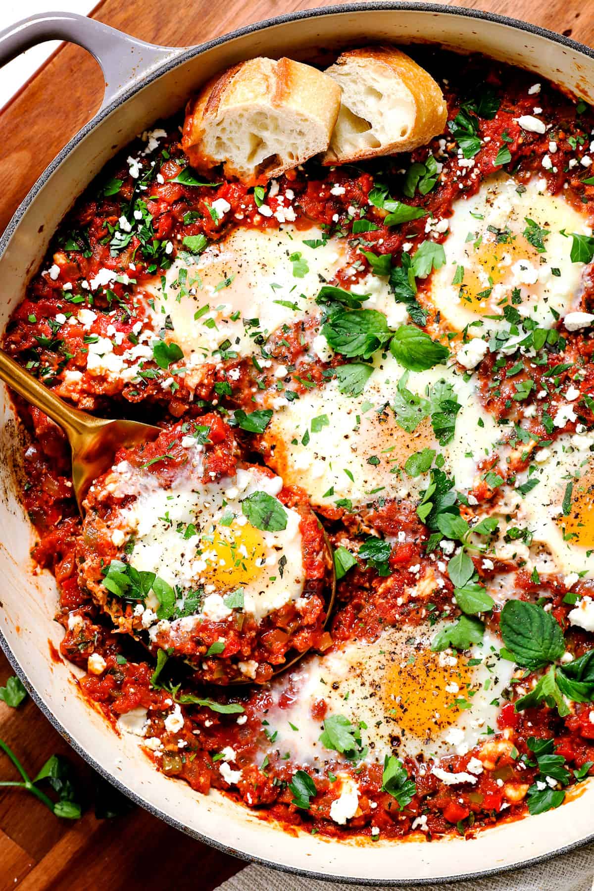 showing how to make shakshuka by garnishing with feta, cilantro and parsley