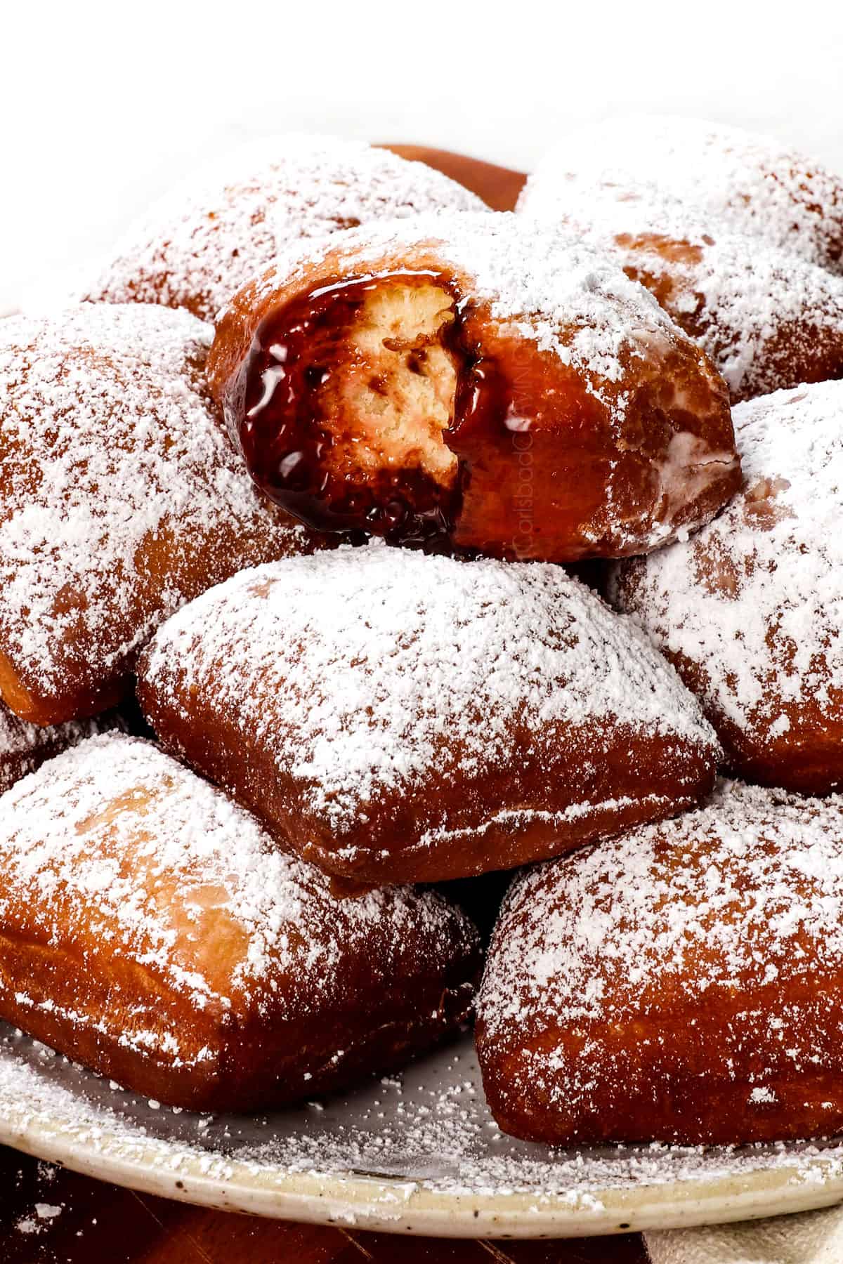 a plate of beignets recipe with a bite taken out of one dipped in chocolate showing how soft and fluffy they are