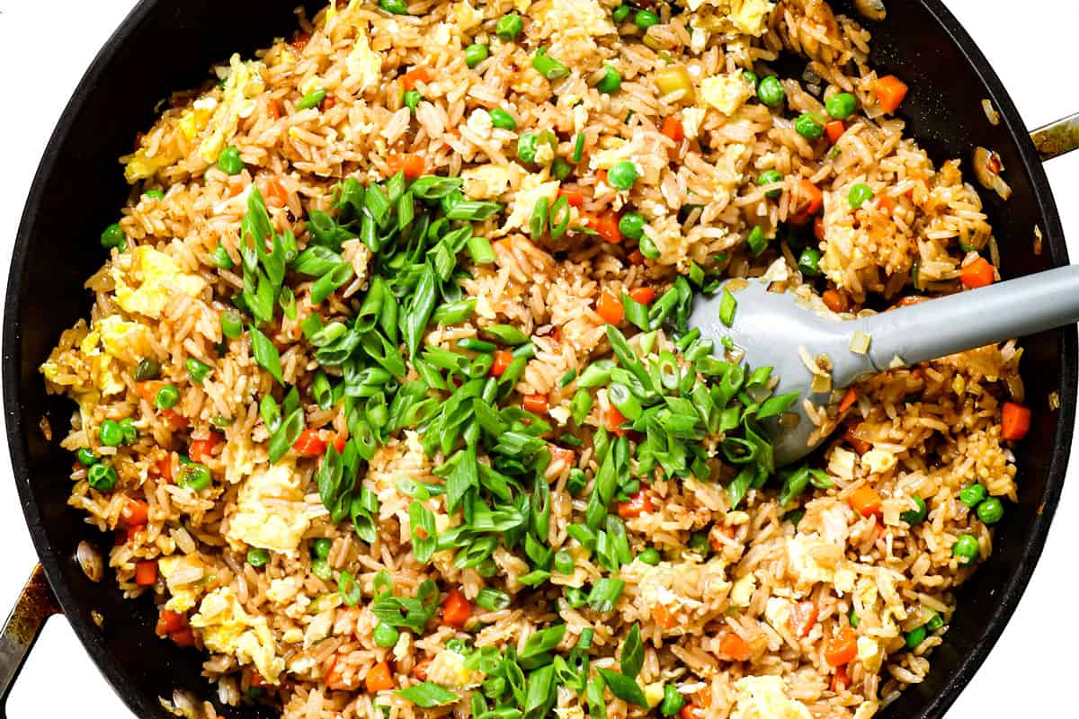 showing how to cook fried rice by stirring green onions into the cooked rice