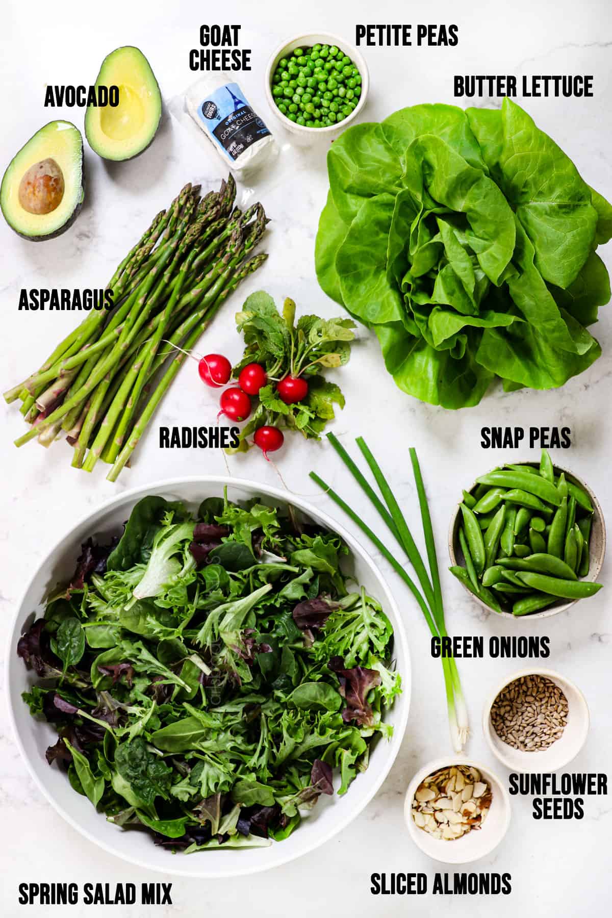 top view of spring salad mix ingredients: spring salad mix, asparagus, peas, radishes, goat cheese, sunflower seeds, almonds and avocados