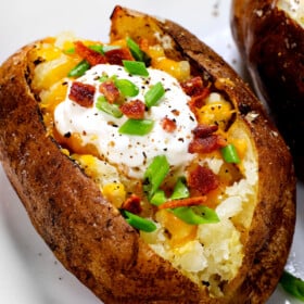 baked potato recipe being served with cheese, bacon, sour cream and green onions