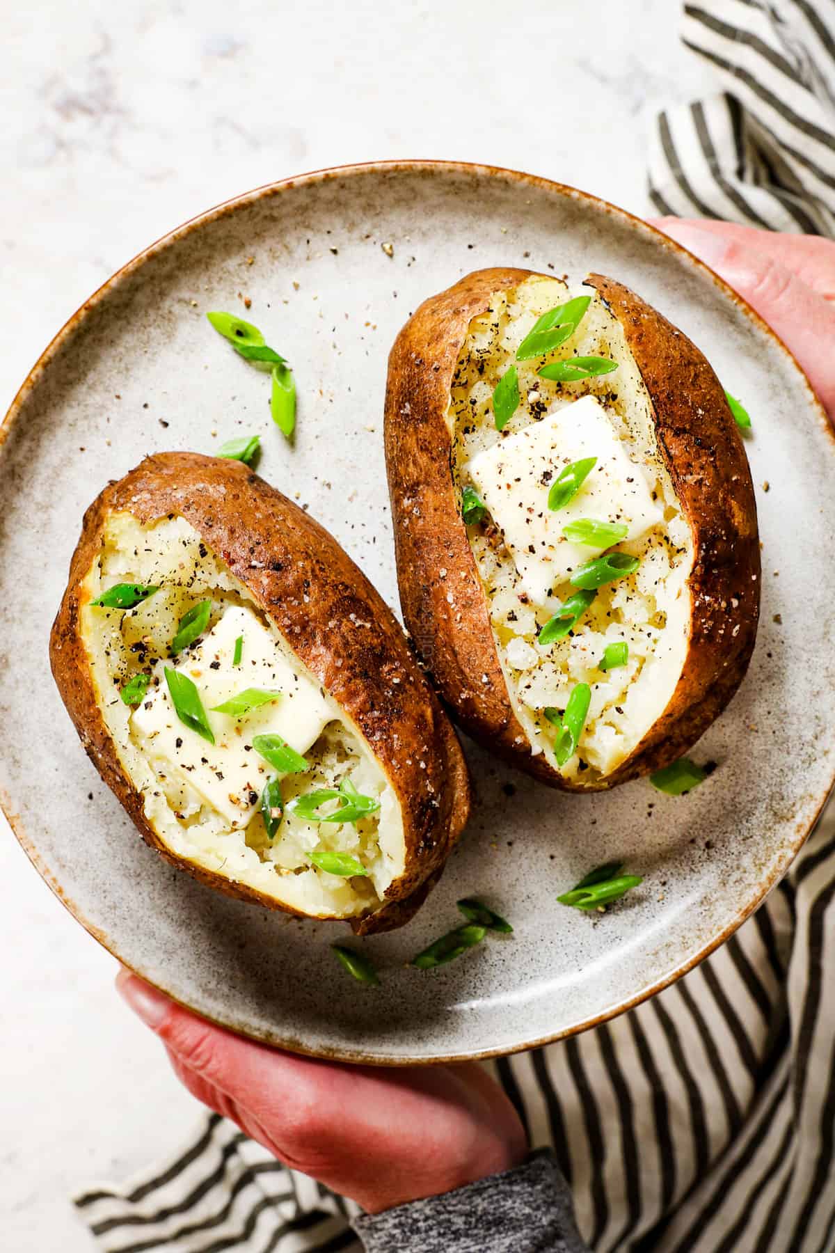 two hand holding baked potato in the oven on a plate