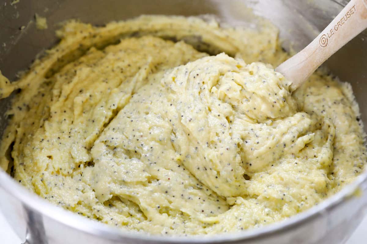 showing how to make lemon poppy seed cake by beating the dry ingredients and wet ingredients into the creamed butter and sugar