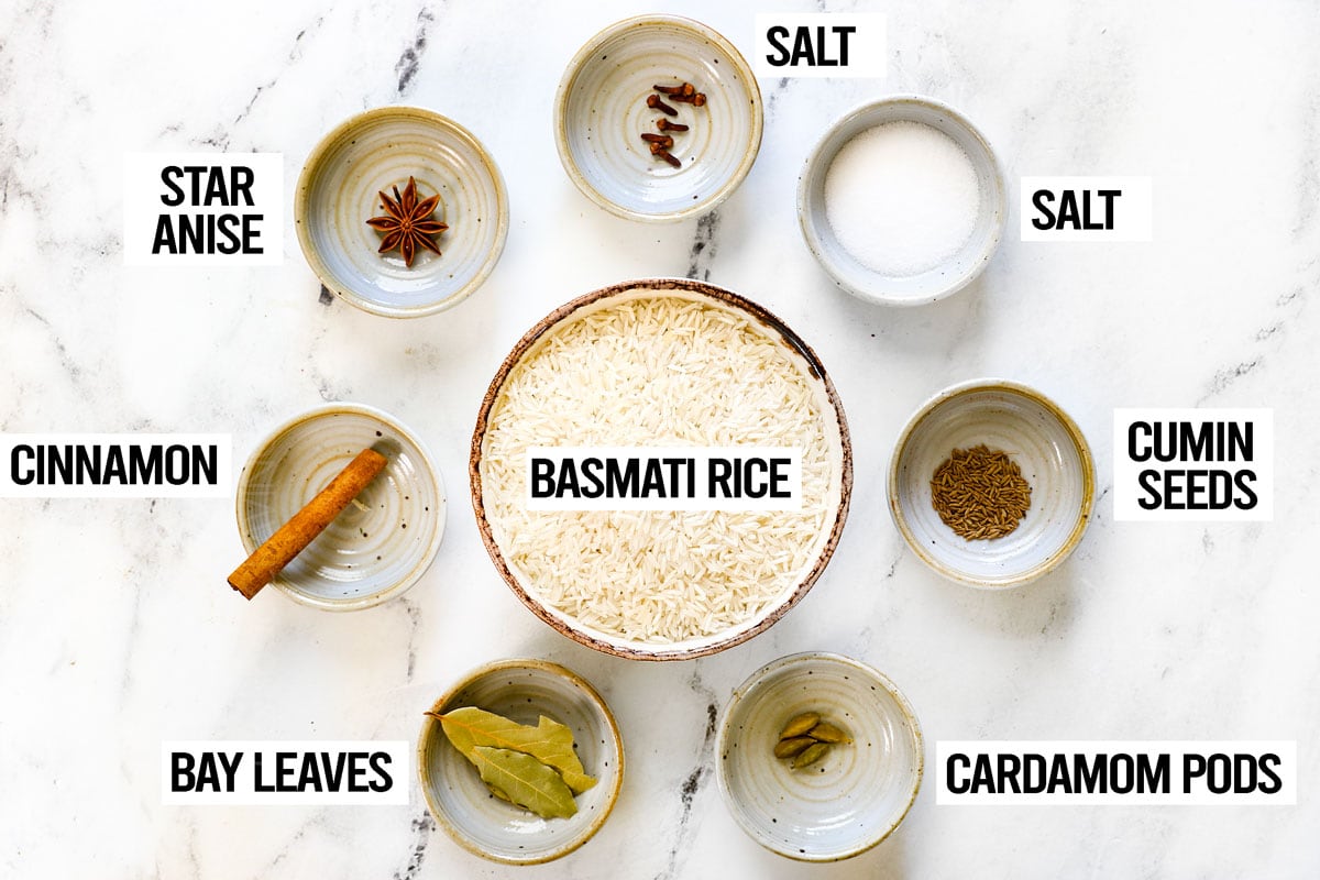 showing rice ingredients for biryani: basmati rice, bay leaves, cinnamon, star anise, cumin seeds, cardamom pods and salt