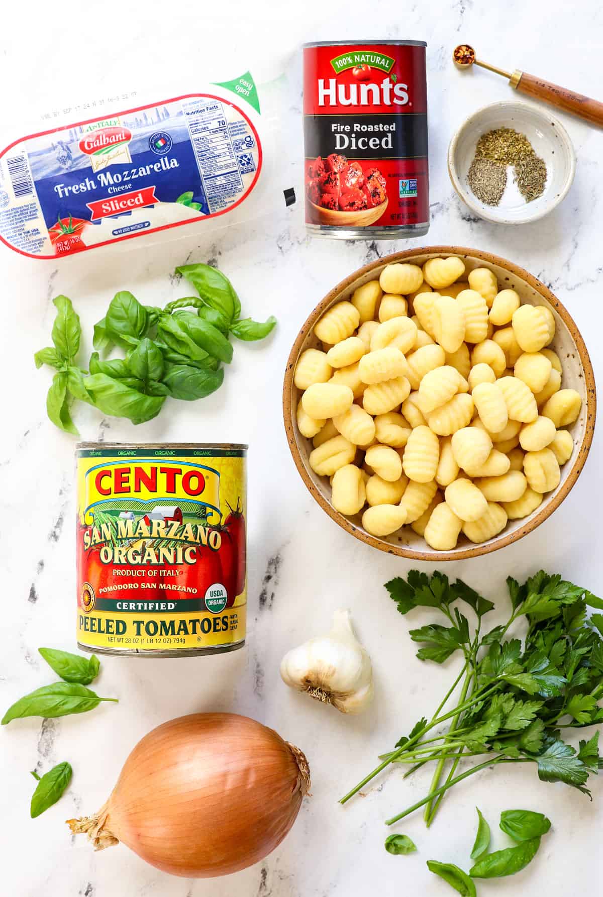 top view of gnocchi recipe ingredients: homemade gnocchi, San Marzano tomatoes, fire-roasted diced tomatoes, fresh mozzarella, fresh basil, fresh parsley, spices, onion, garlic and red pepper flakes