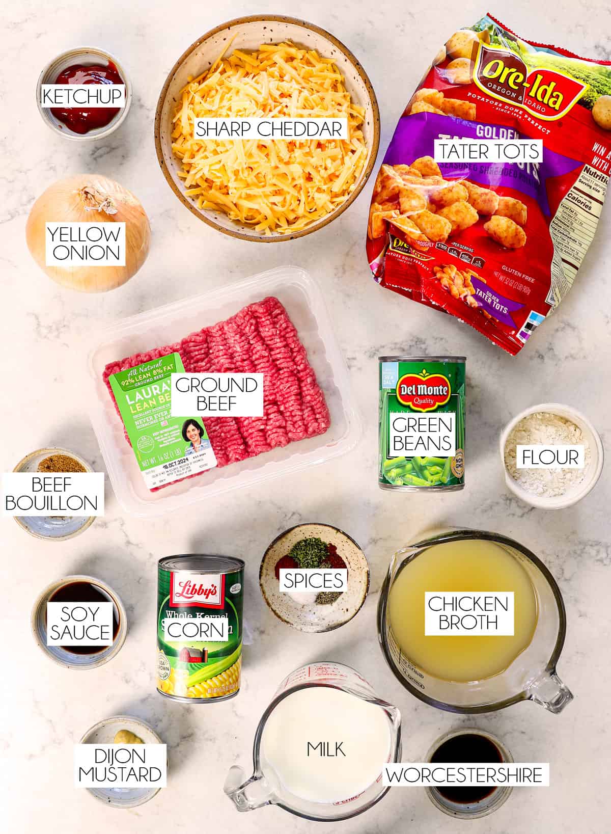 top view of tater tot casserole ingredients: ground beef, tater tots, cheese, green beans, corn peas, chicken broth, milk, flour, ketchup, soy sauce, Worcestershire sauce, and spices