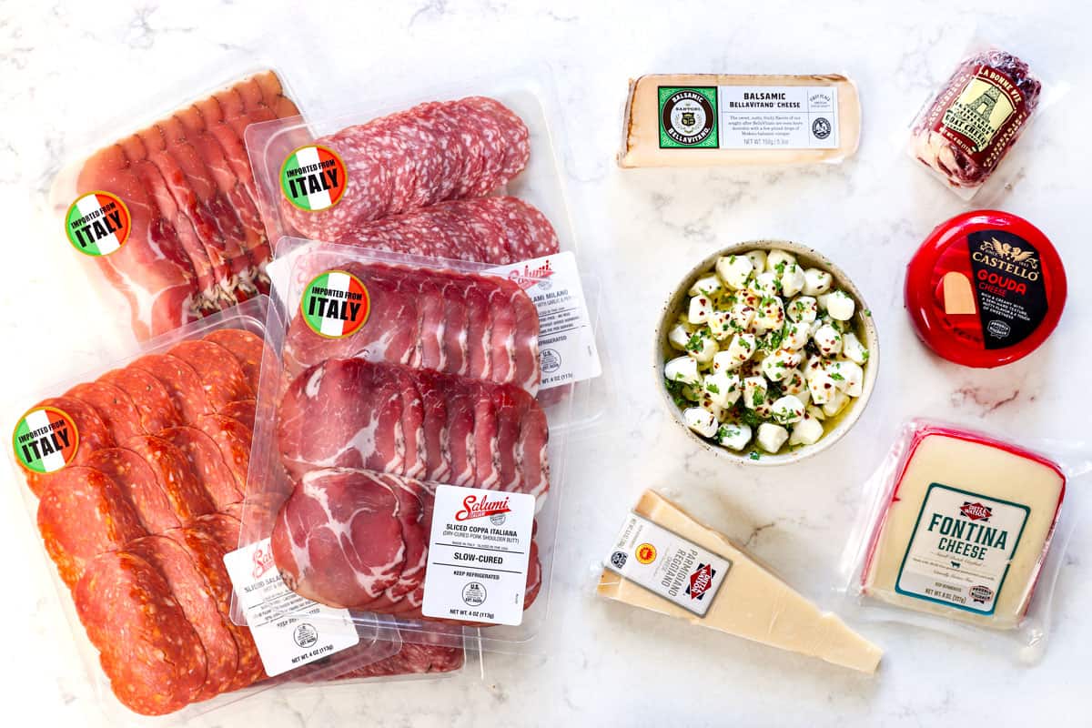 top view showing meats and cheeses for antipasto platter: • Parmigiano Reggiano, Provolone, Fontina, Balsamic BellaVitano, marinated mozzarella balls, cheese log, Genoa salami, Soppressata, prosciutto, dried coppa