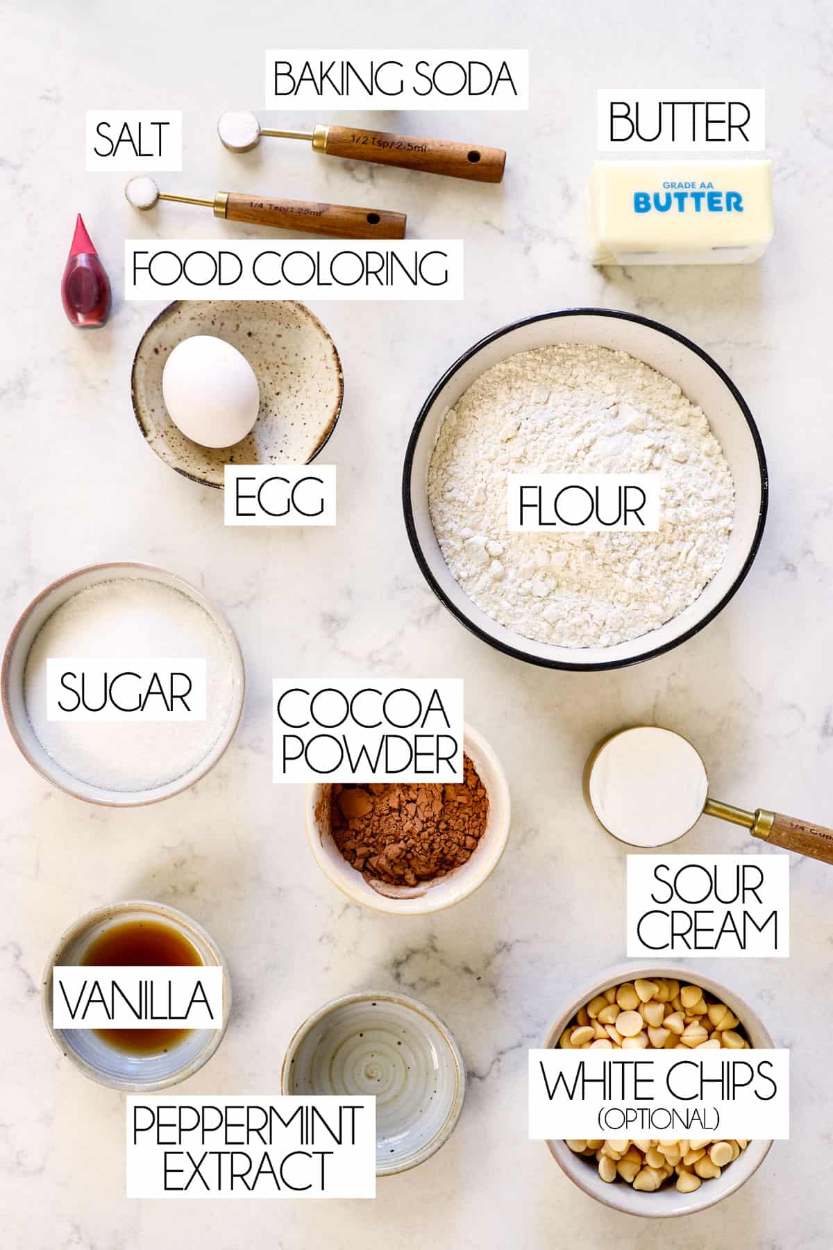 top view of red velvet cookie ingredients: flour, sugar, cocoa powder, vanilla, egg, baking soda, salt, butter, food coloring