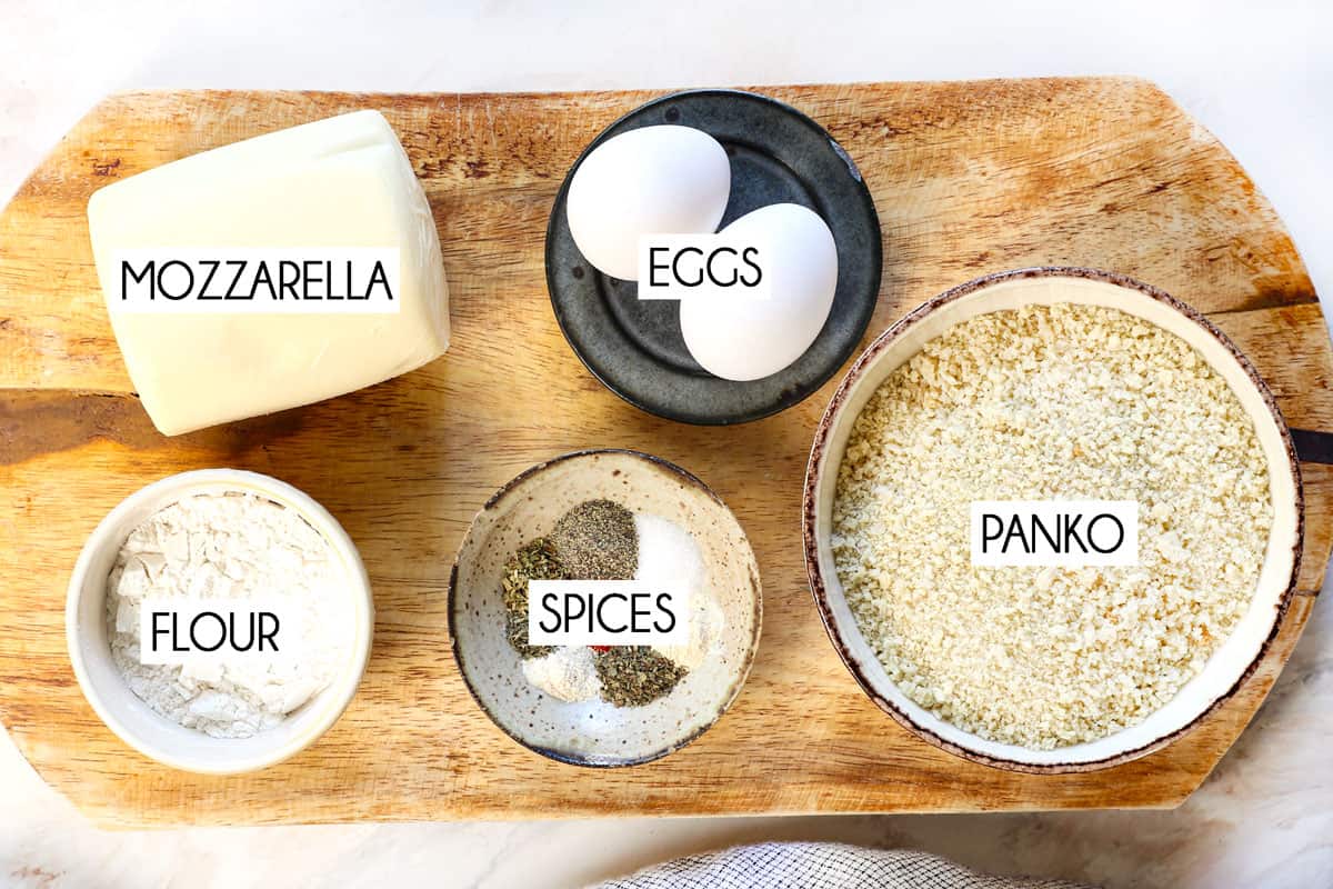 top view showing ingredients of mozzarella sticks: mozzaralle block, panko, eggs, spices and flour