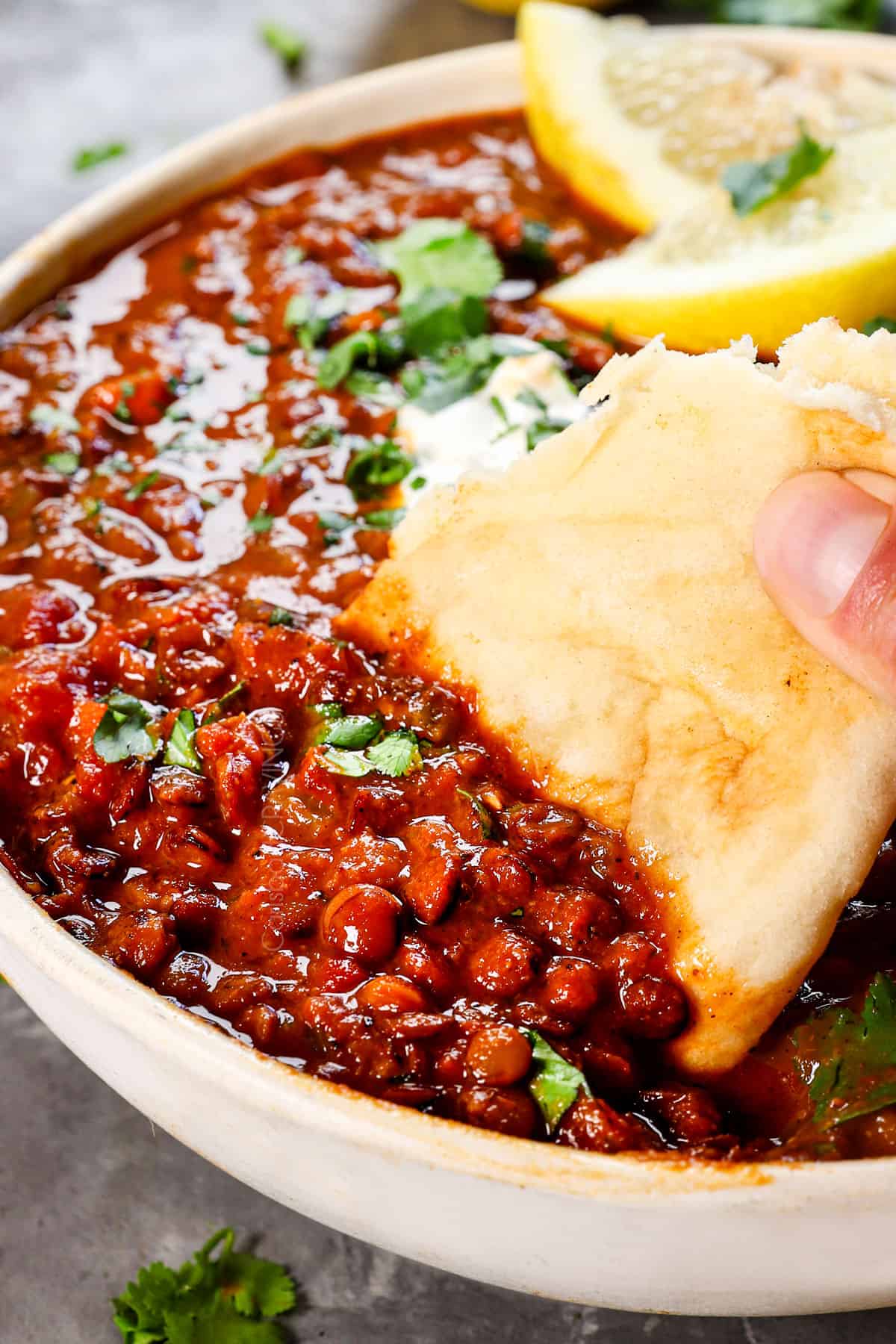 showing how to serve lentil soup by scooping it up with naan