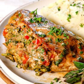 up close of serving baked stuffed chicken breast on a plate with mashed potatoes and asparagus