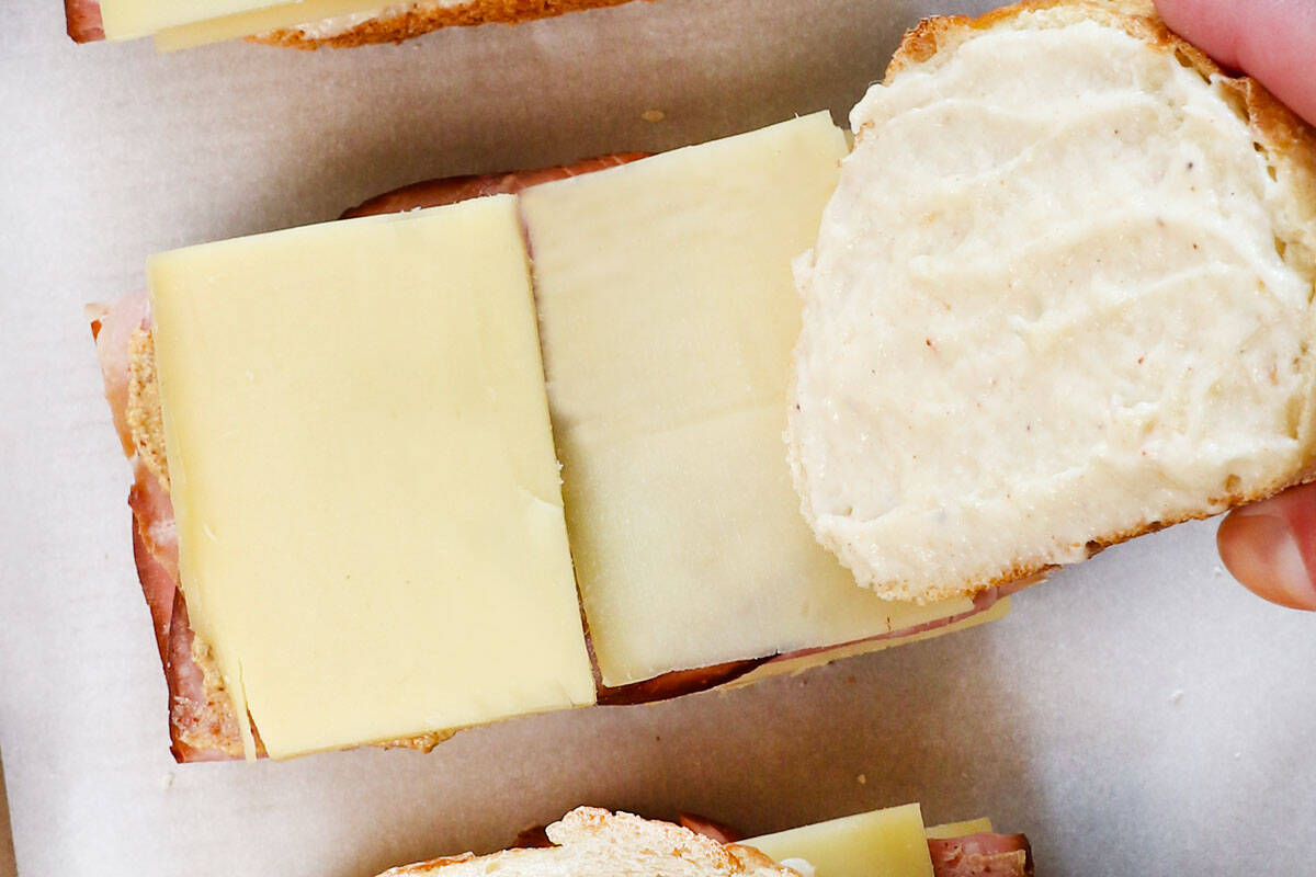 showing how to make croque monsieur by topping the sandwich a piece of bread, béchamel side down