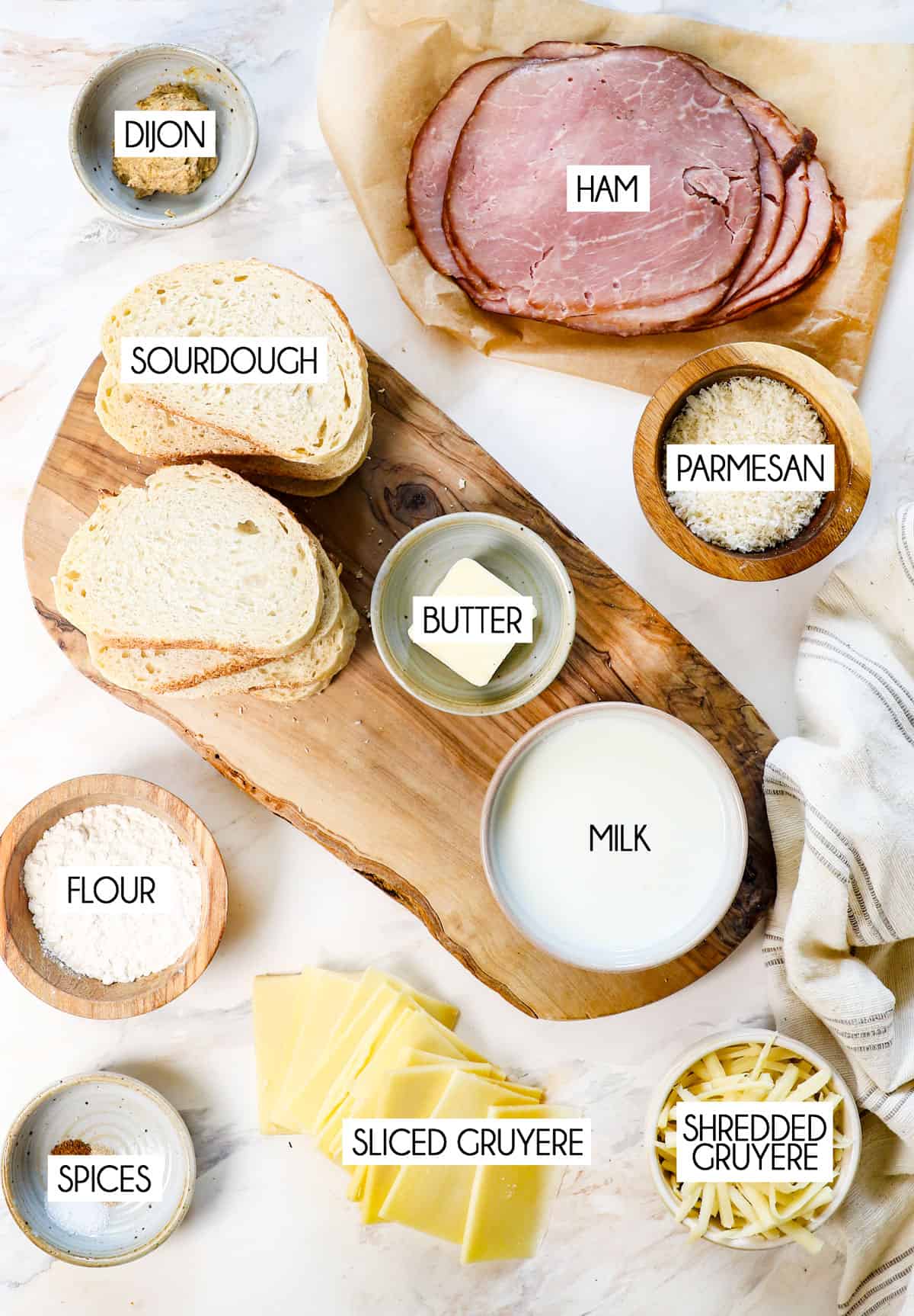 top view of croque monsieur ingredients: sourdough bread, ham slices, Gruyere swiss cheese, flour, milk, nutmeg, white pepper, Dijon mustard