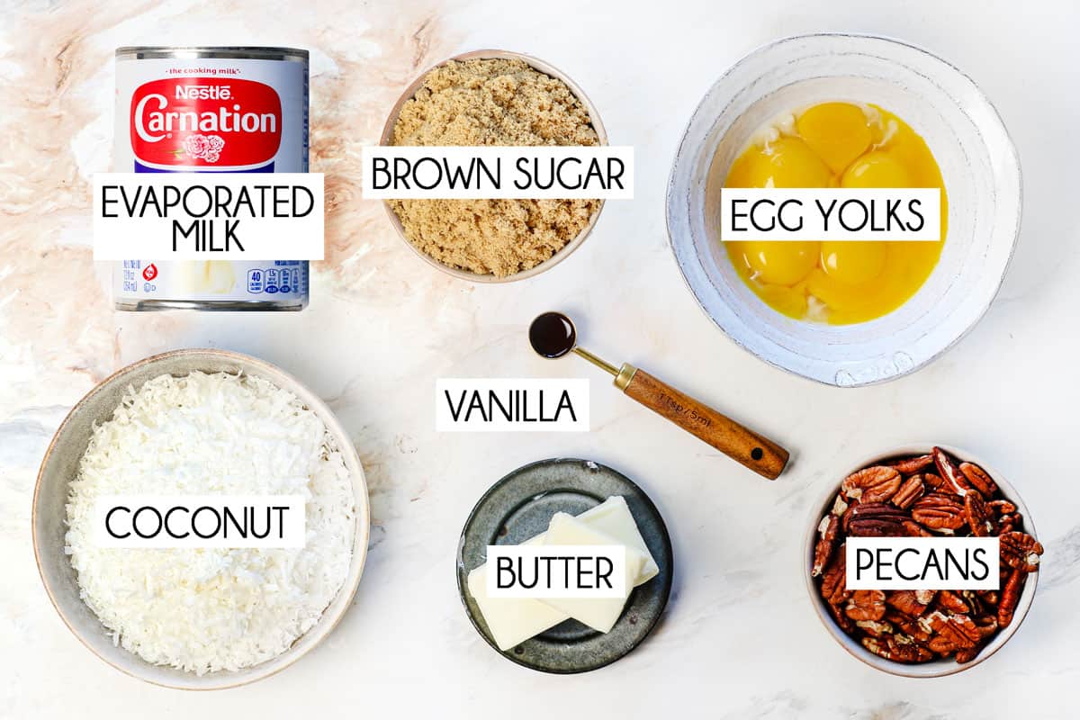 Top view of German chocolate cake frosting ingredients: evaporated milk, brown sugar, egg yolks, coconut, butter, pecans, vanilla