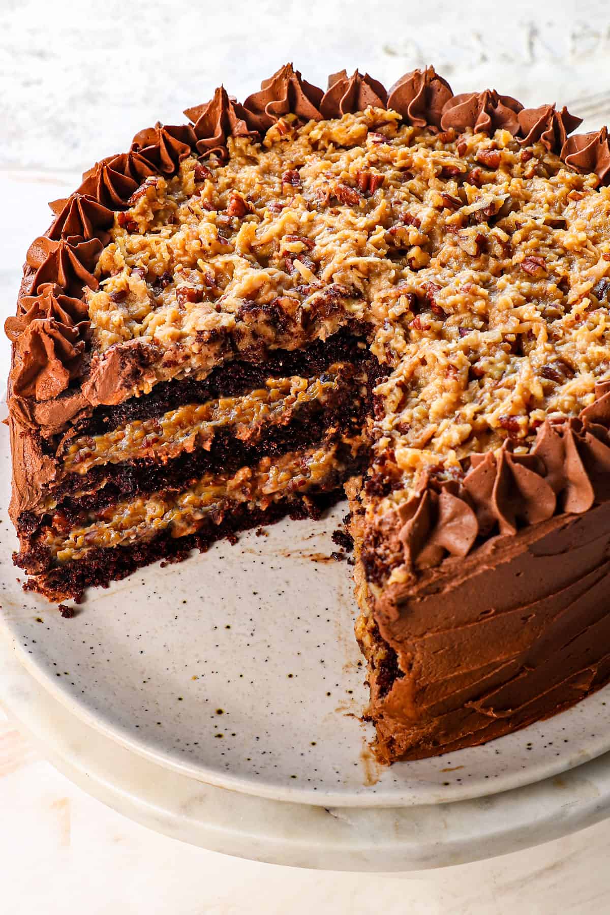 recipe for german chocolate cake with a few pieces removed showing the stacks of cake, German chocolate frosting, cake, German chocoalte frosting, cake, then topped with German chocolate frosting