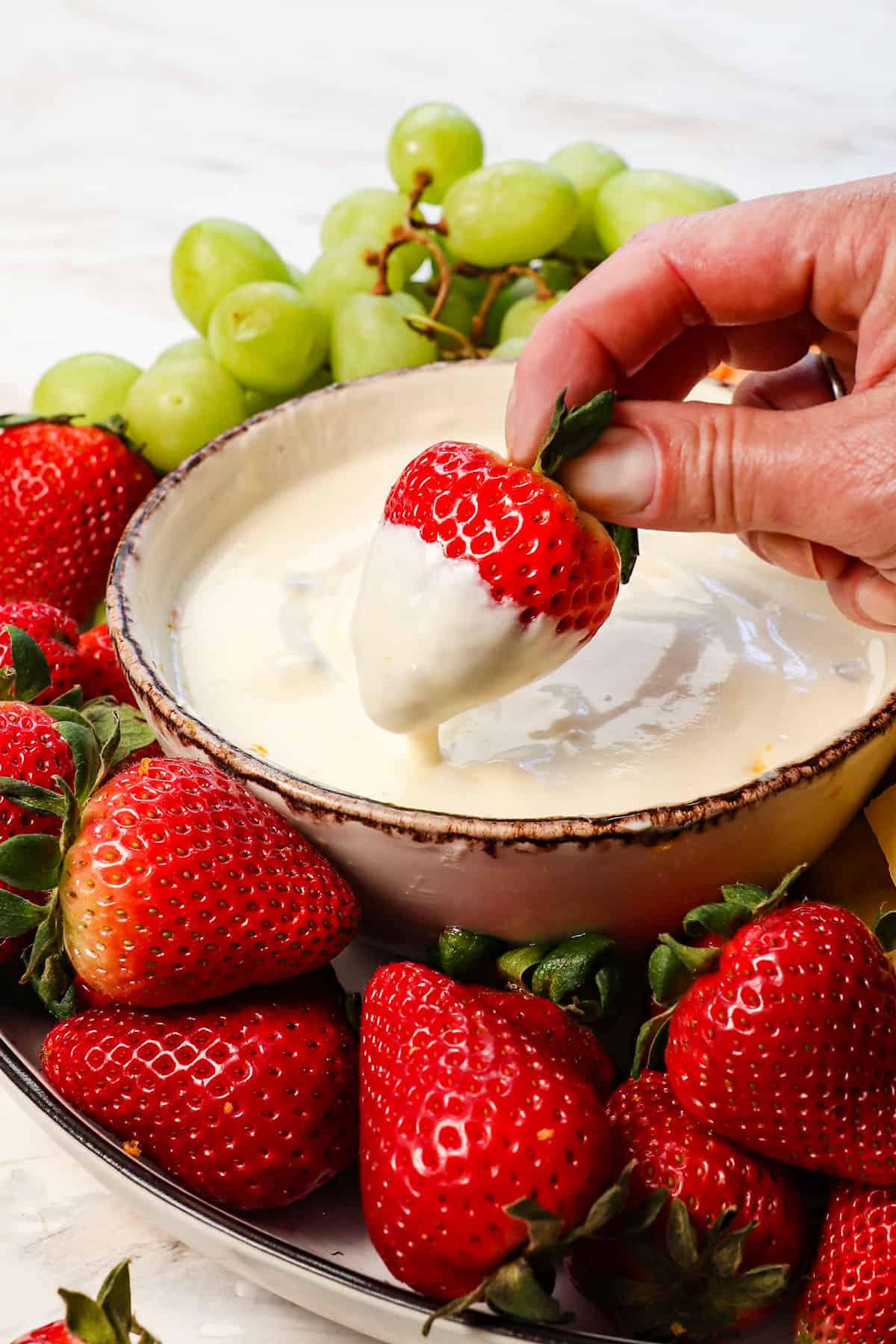 up close of dipping a strawberry in fruit dip with cream cheese showing how creamy it is