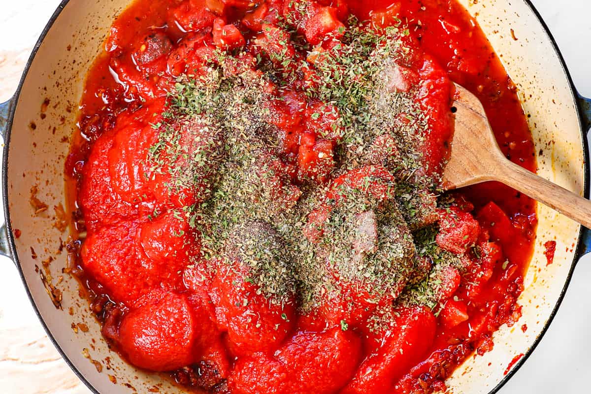 showing how to make pink sauce by stirring in the crushed tomatoes, fire-roasted diced tomatoes, bouillon, spices, and bay leaf.