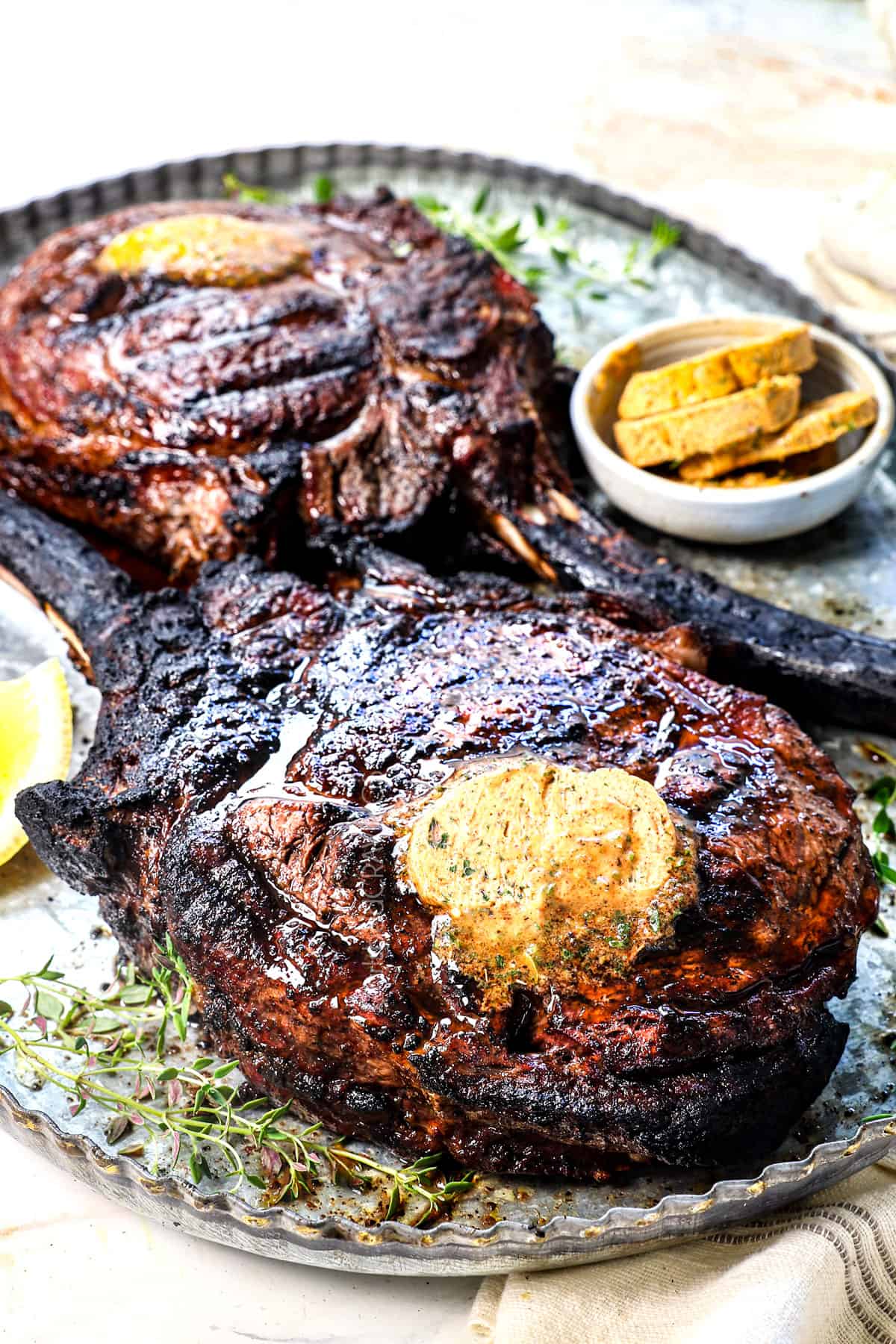 showing how to cook tomahawk steak by adding the compound butter on top after cooking, and letting the steaks rest before slicing