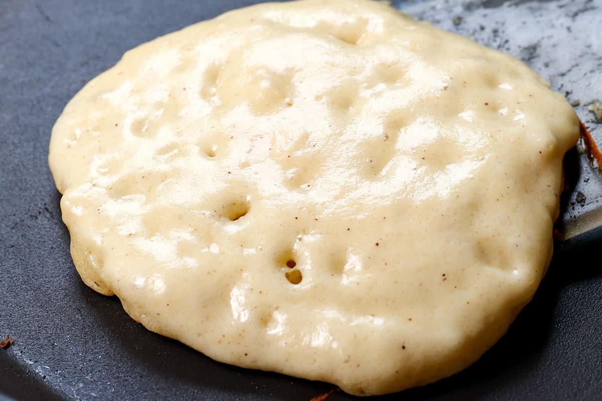 showing how to make homemade pancakes that are fluffy by cooking the pancakes in a skillet, and flipping when a few bubbles appear are on the surface