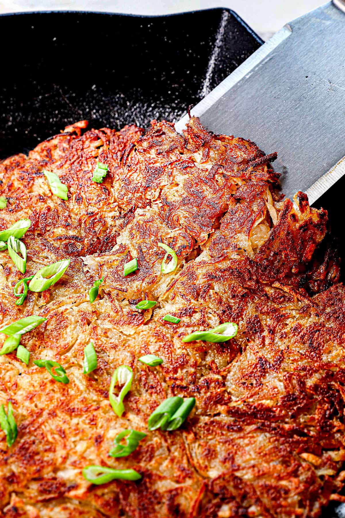 a spatula lifting up hash brown recipe in a skillet showing how golden and crispy it is