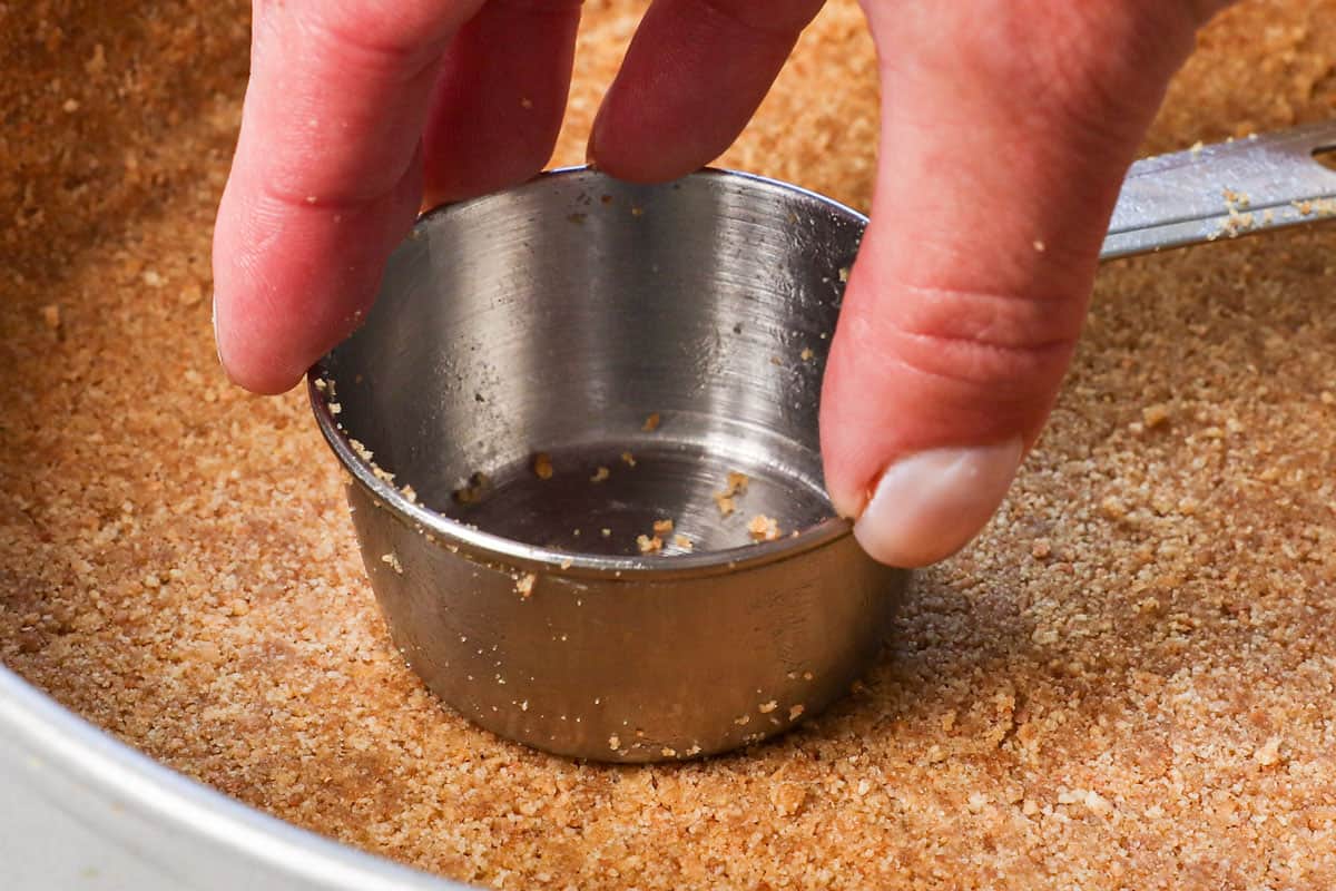 showing how to make no bake cheesecake by pressing the crust up the sides and the bottom of a springform pan