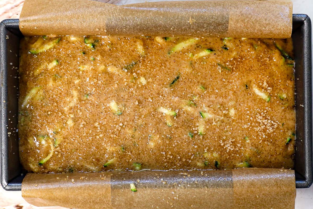 showing how to make zucchini bread by pouring the batter into a loaf pan lined with parchment paper