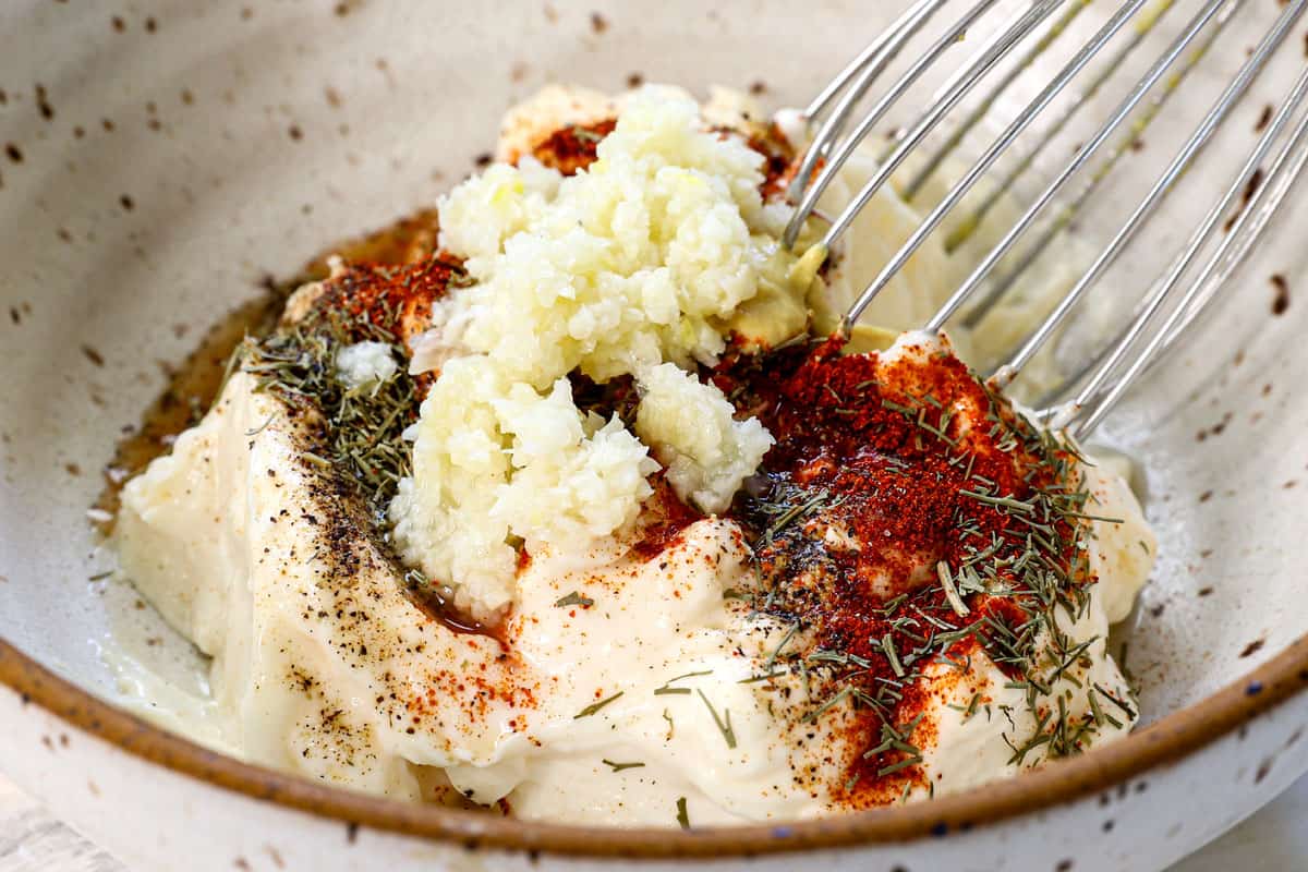 showing how to make garlic aioli by stirring the mayonnaise, garlic, lemon juice, Dijon mustard, paprika, salt and pepper together in a bowl
