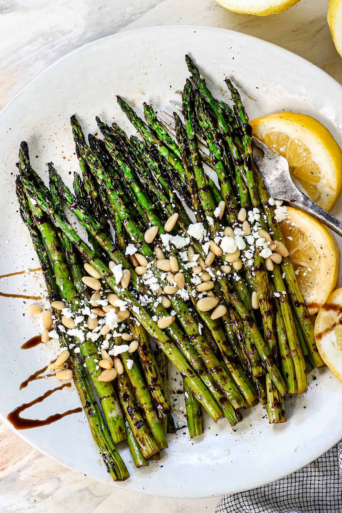 top view showing how to serve grilled asparagus recipe garnished by nuts, cheese, and lemon