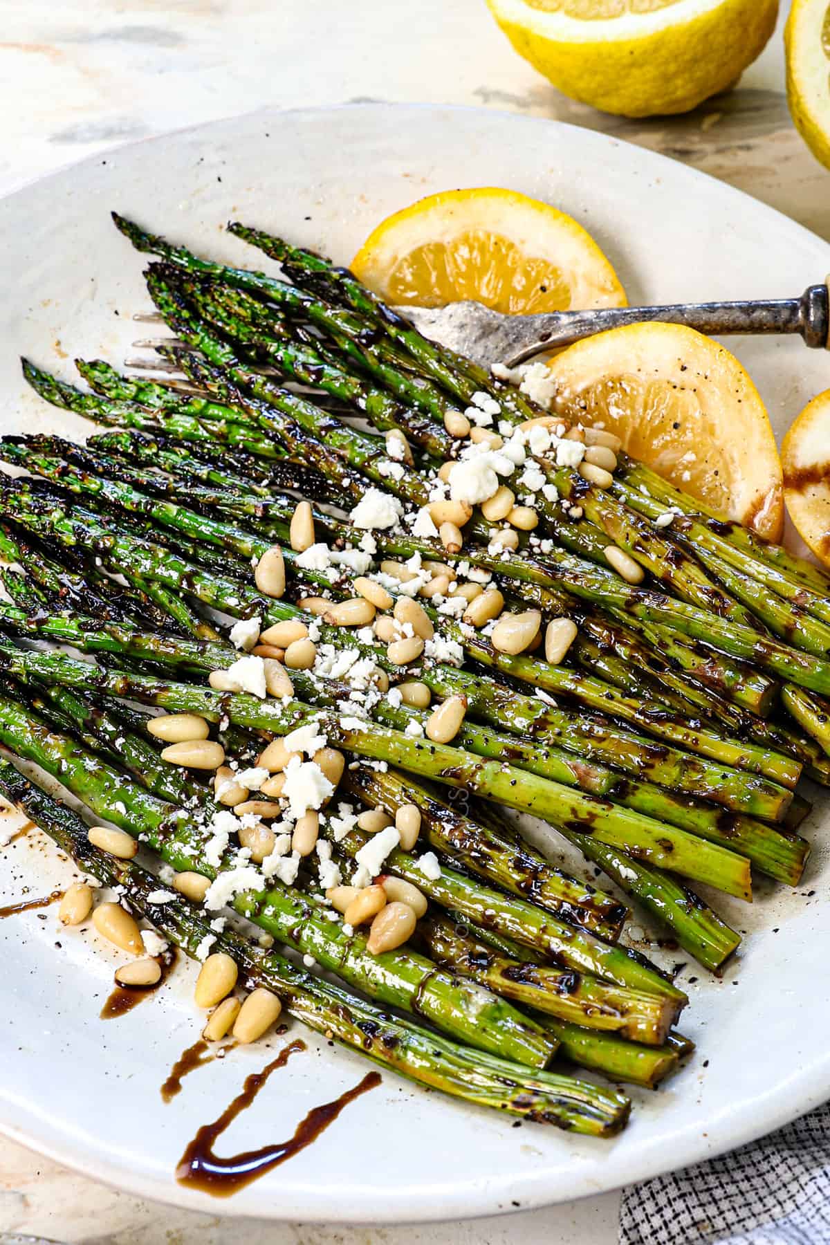showing how to serve grilled asparagus with balsamic reduction, pine nuts and goat cheese