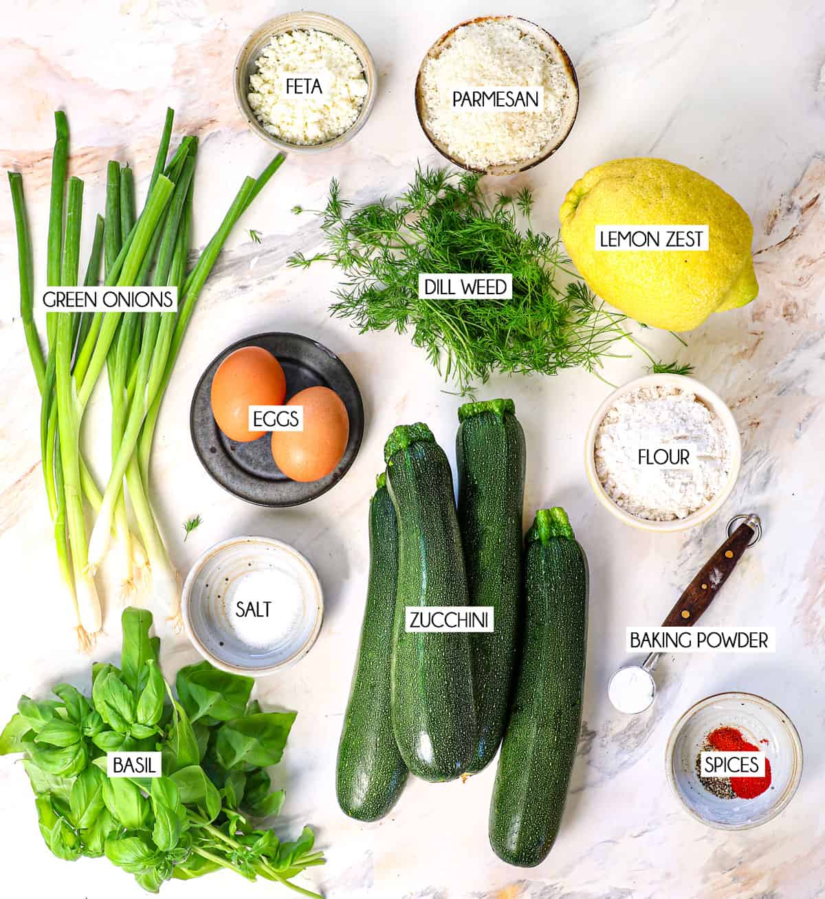top view of zucchini fritter ingredients: zucchini, flour, baking powder, eggs, salt, Parmesan, dill weed, lemon zest, green onions, basil, spices, panko