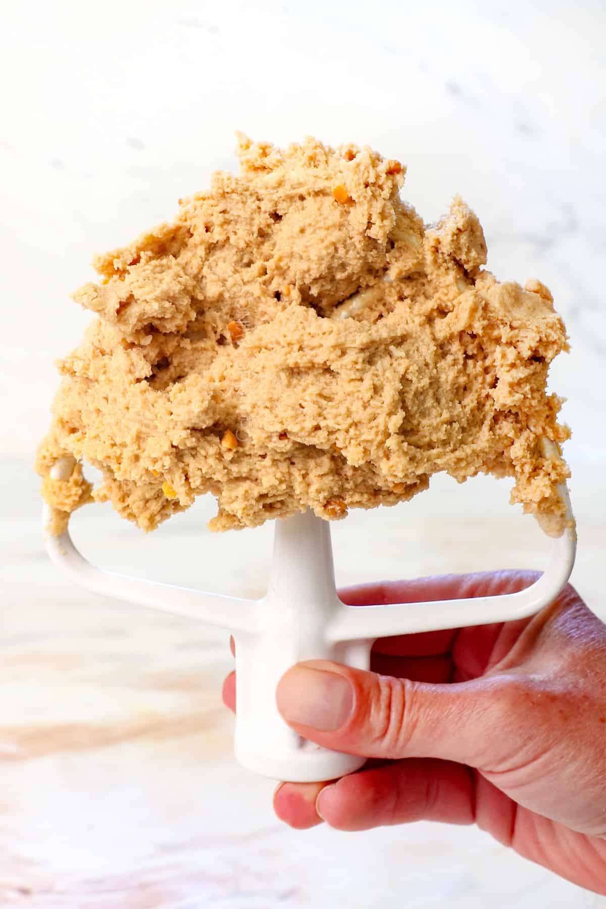 holding up a paddle attachment of homemade edible cookie dough showing the thick consistency