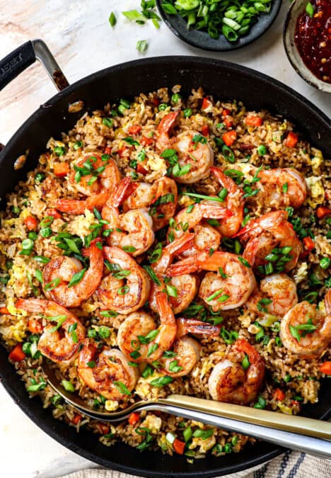 showing how to make shrimp fried rice by garnishing with green onions and seasoning to taste