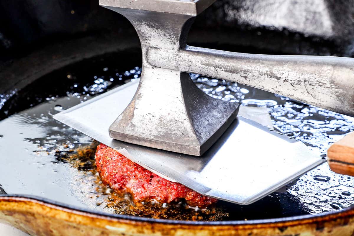 showing how to make smash burgers by covering the ground beef ball with parchment paper, then smashing it down with a metal spatula