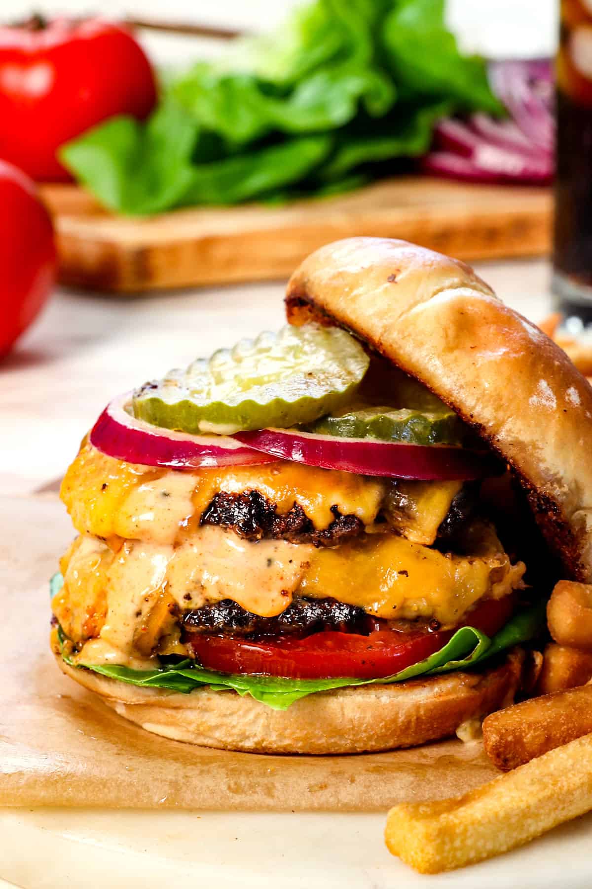 showing how to make smash burgers by assembling the burgers on buns with lettuce tomatoes, cheeseburger stack, red onions and pickles