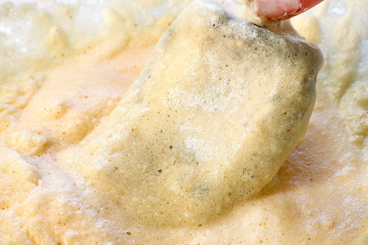 showing how to make chile rellenos by dipping the poblano pepper in the batter until coated