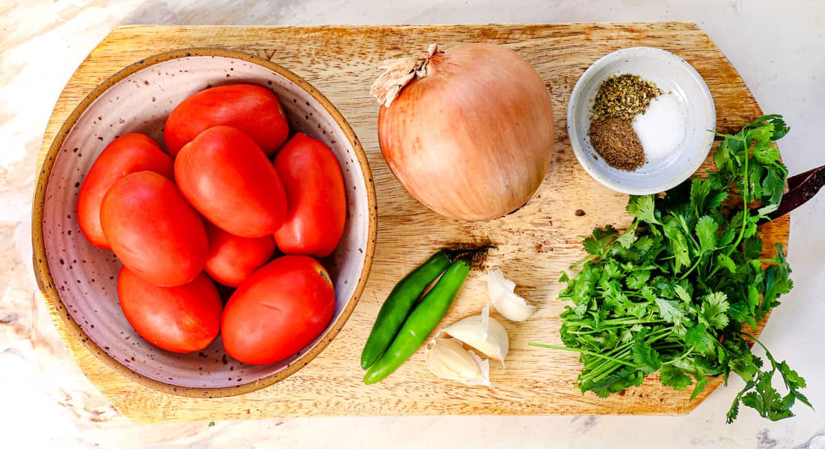 top view of chile relleno ingredients for the salsa: Roma tomatoes, yellow onion, garlic, cilantro and serrano chili peppers