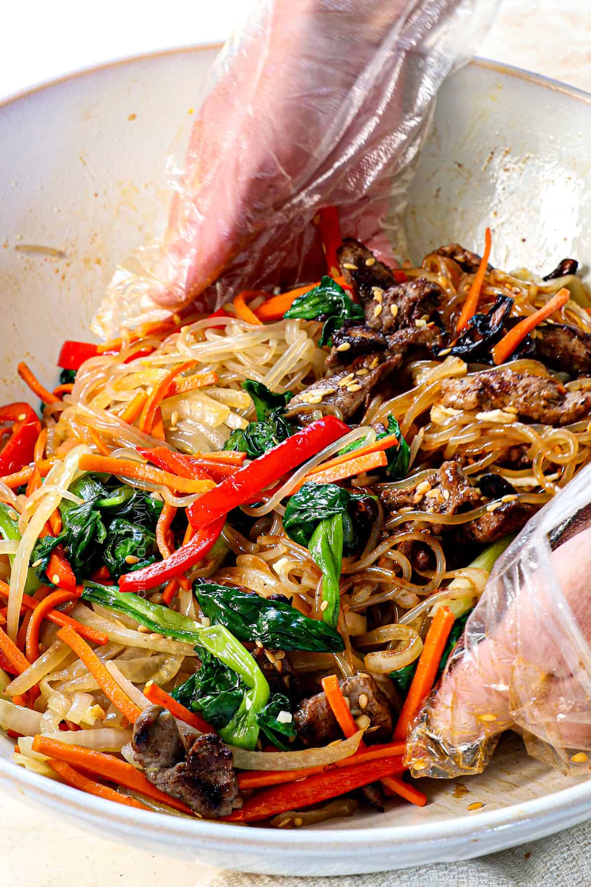 tossing Japchae recipe ingredients together with gloved hands