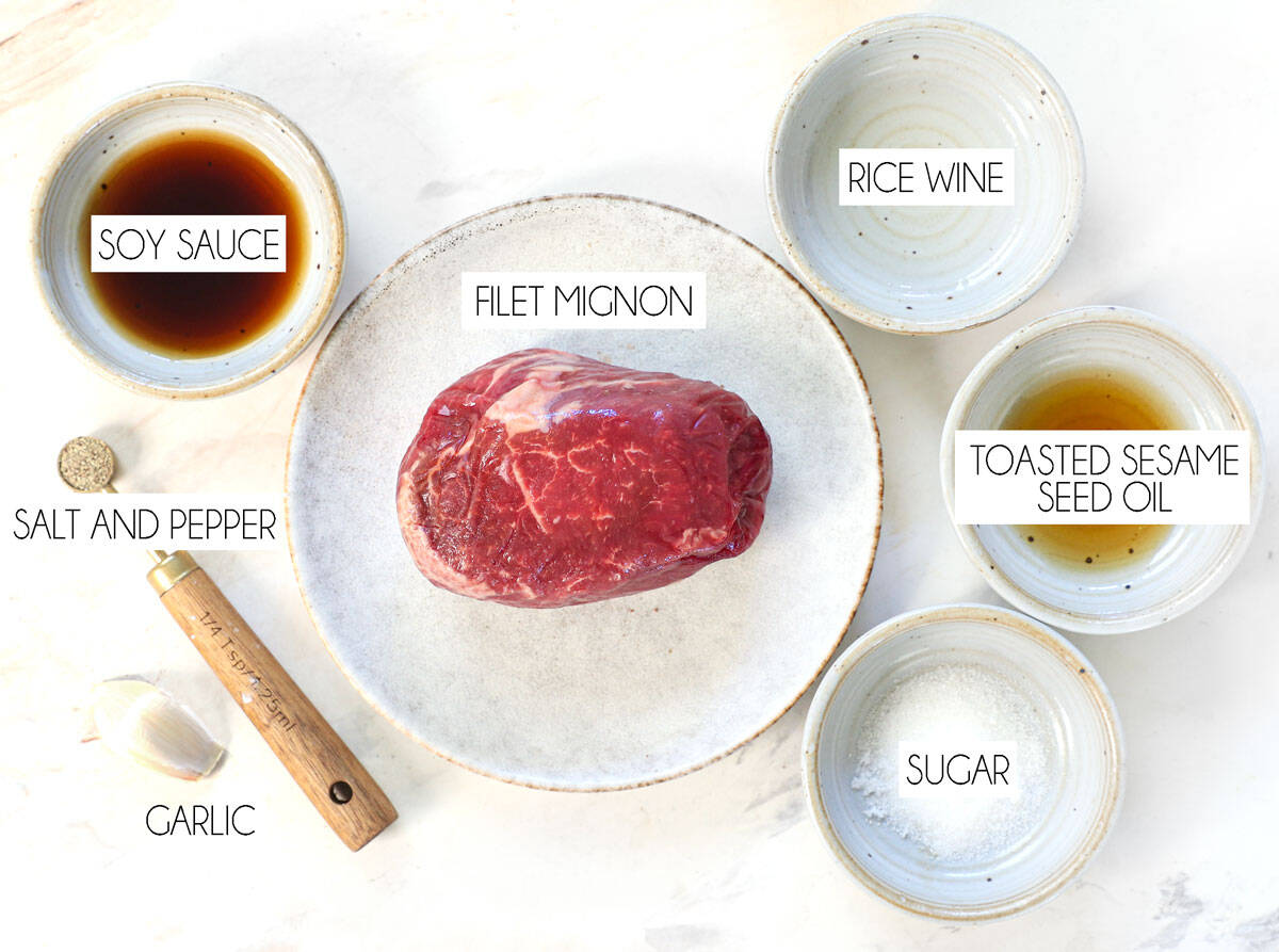 top view of japchae ingredients for the beef marinade: filet mignon, soy sauce, toasted sesame seed oil, rice wine, sugar, salt, and garlic