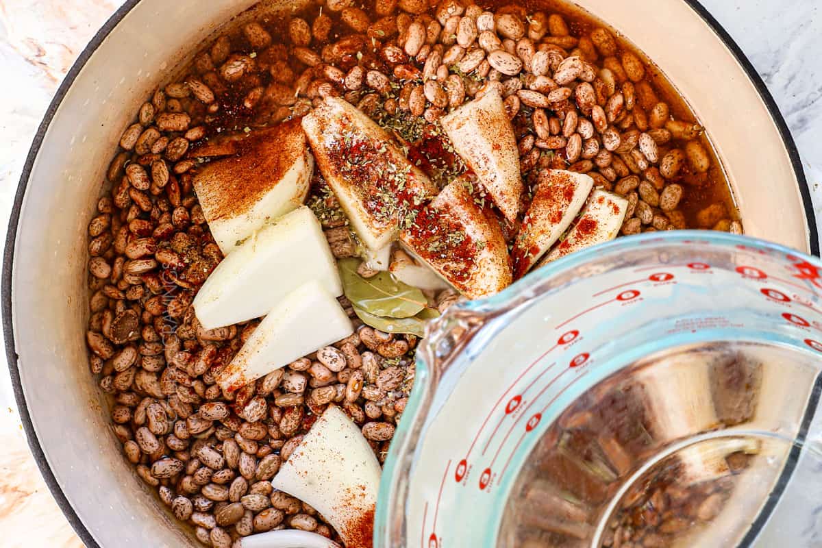 showing how to make refried beans by adding the beans, onion wedges, bay leaves, spices and water to a Dutch oven