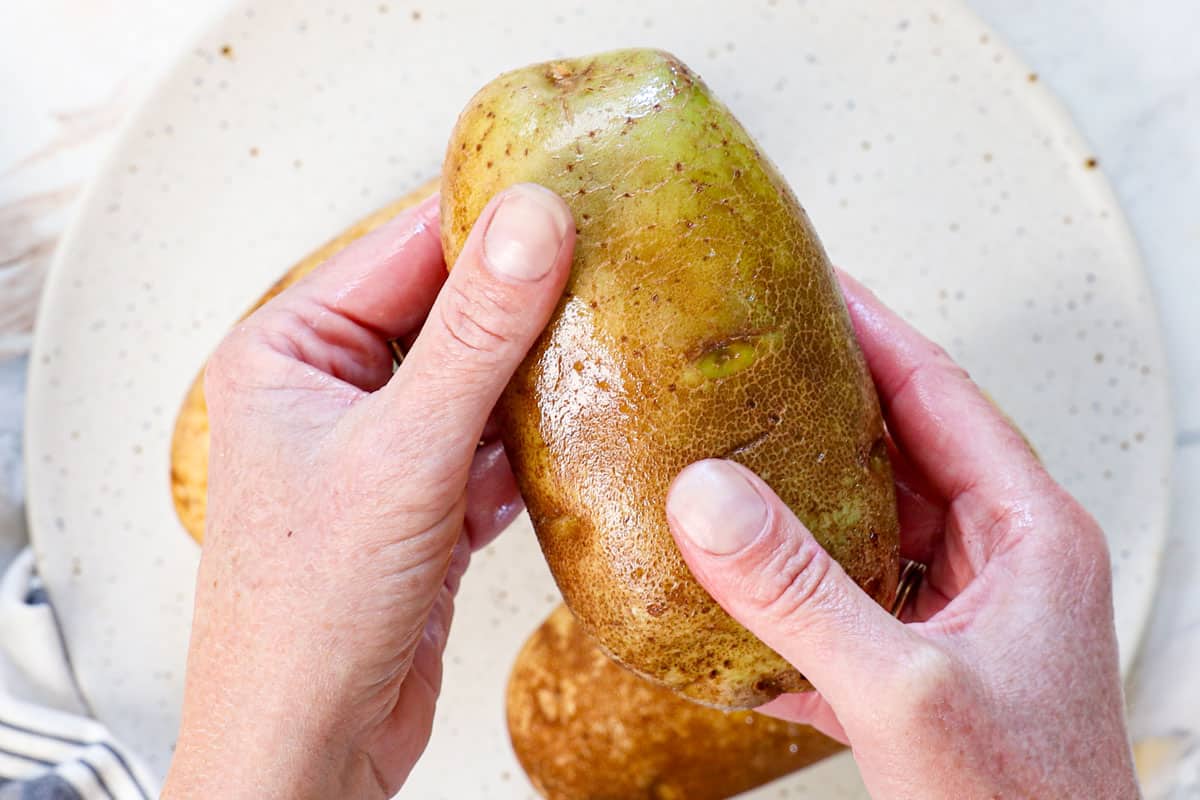 showing how to make baked potatoes in air fryer by drizzling the potatoes with oil and rubbing the oil all over