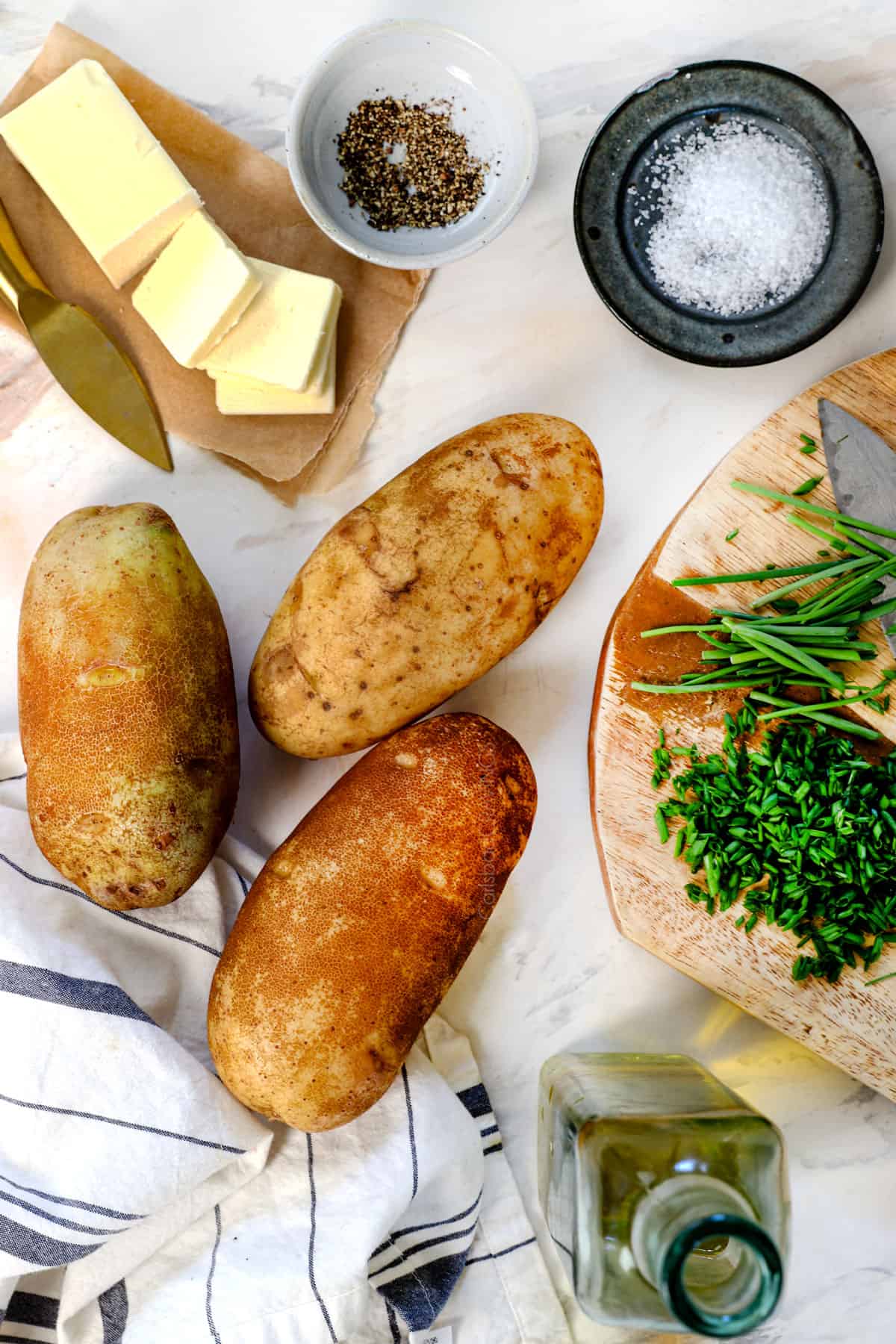 top view of air fryer baked potato ingredients: russet potatoes, butter, salt, pepper, chives