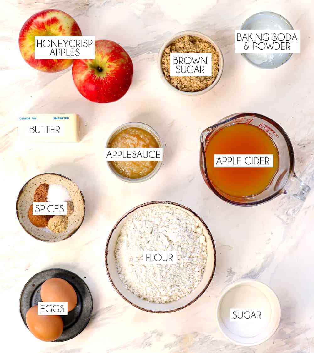 top view of apple cider donut recipe ingredients: apple cider, apples, applesauce, flour, brown sugar, white sugar, eggs, spices, baking soda, baking powder, butter