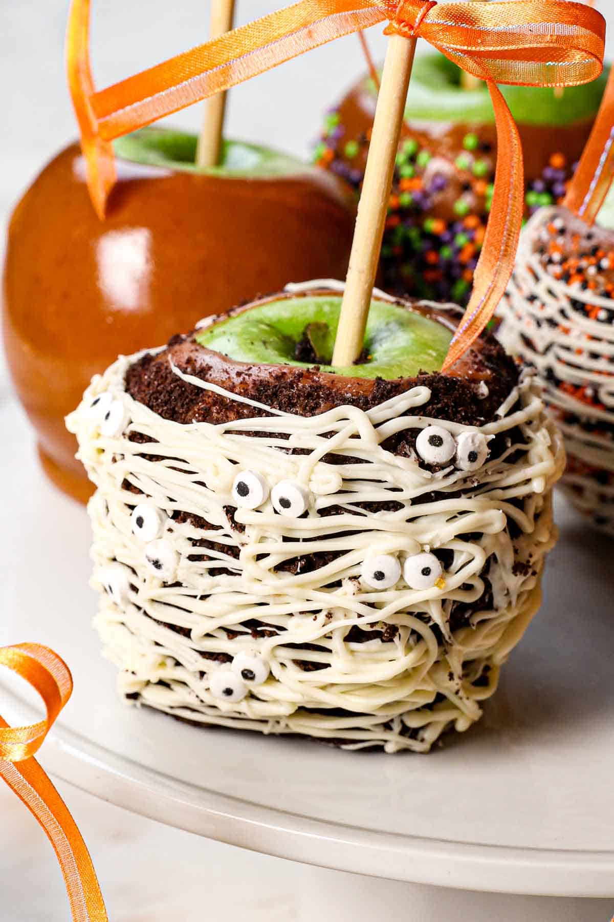 up close showing how to decorate caramel apples with crushed cookies (Oreos) and chocolate